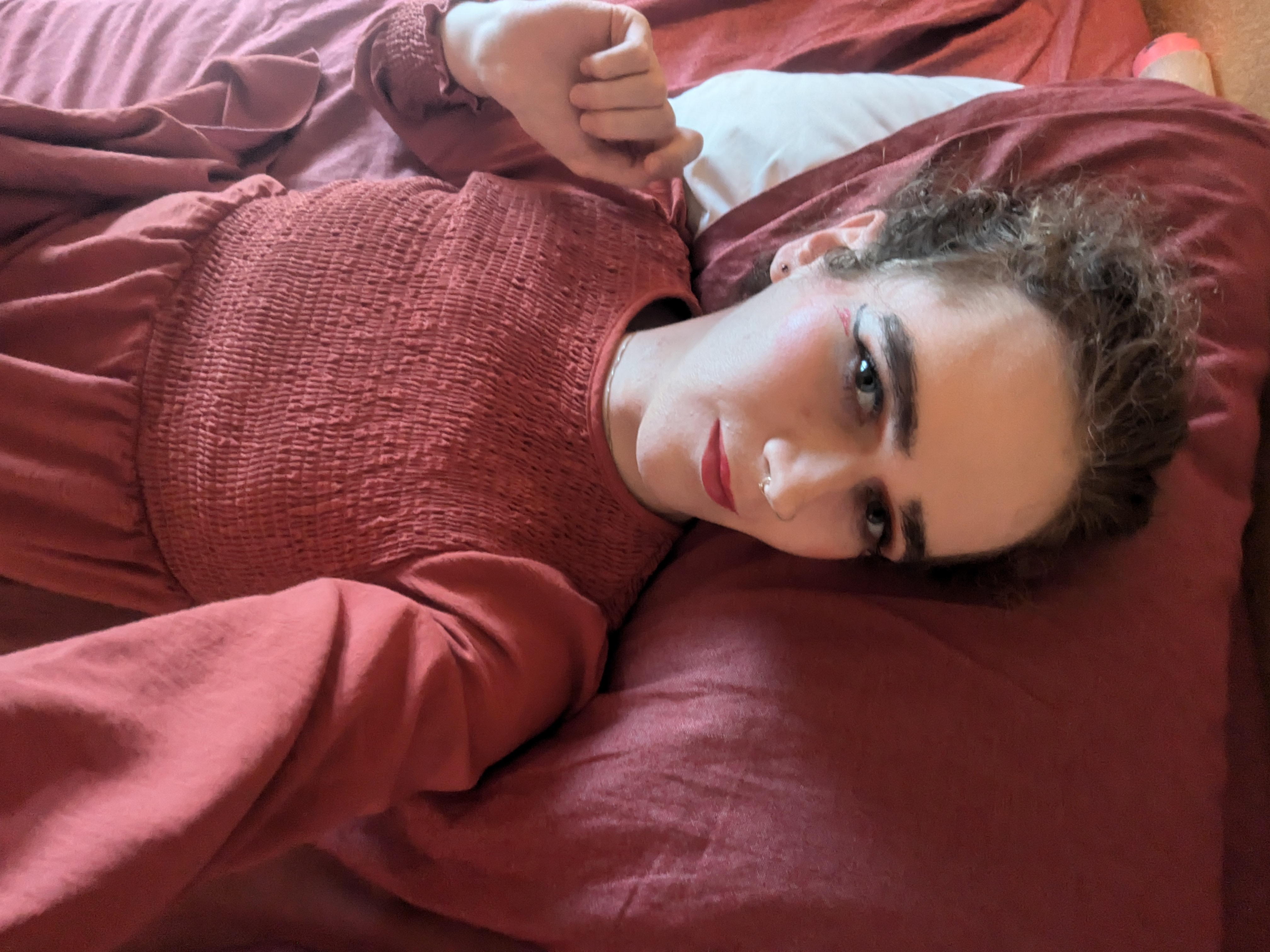 The photo shows a woman lying down on a bed with red bedding,... - by Daisy