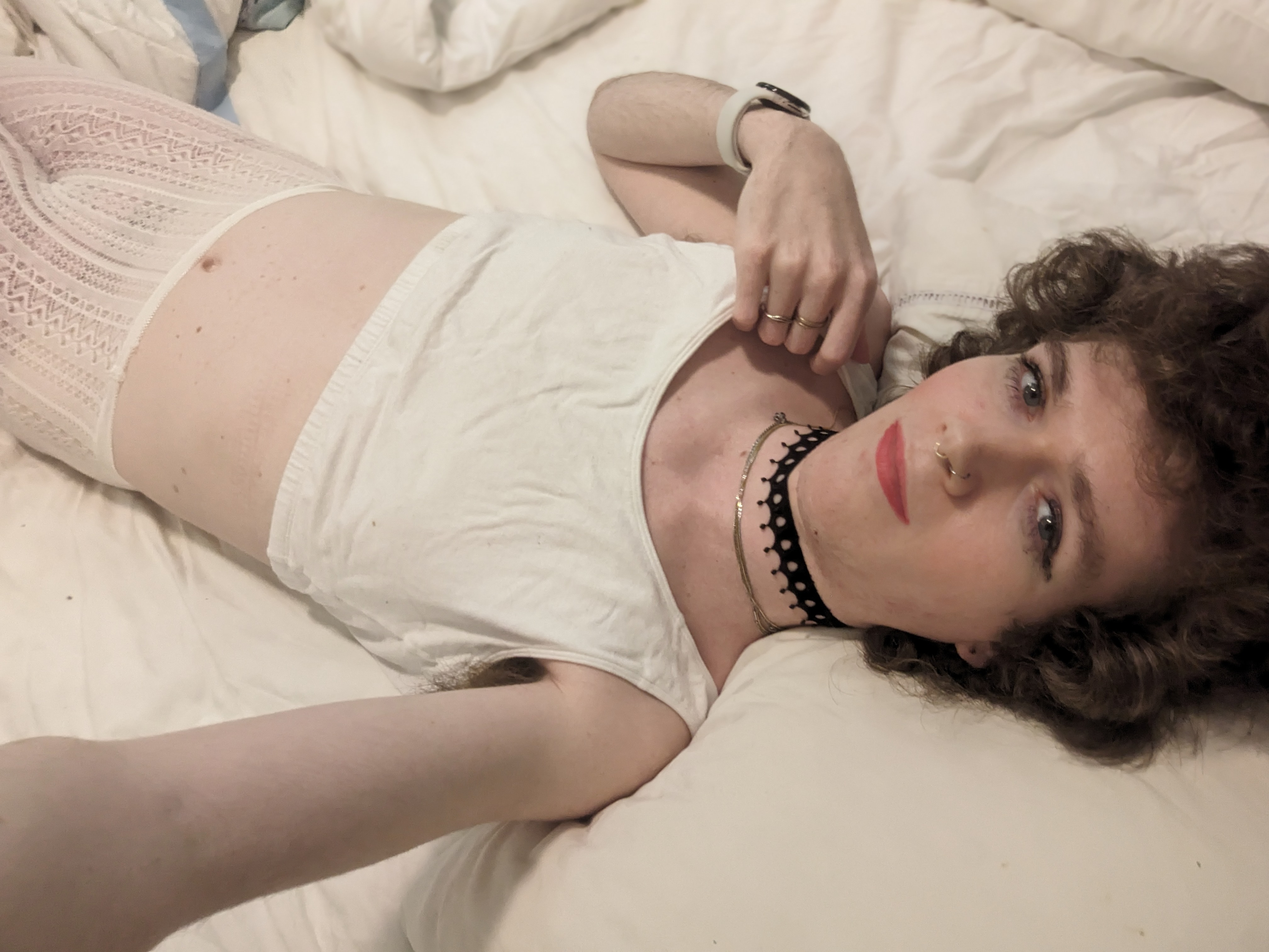 The photo shows a woman lying on a bed, wearing a white crop top... - by Daisy