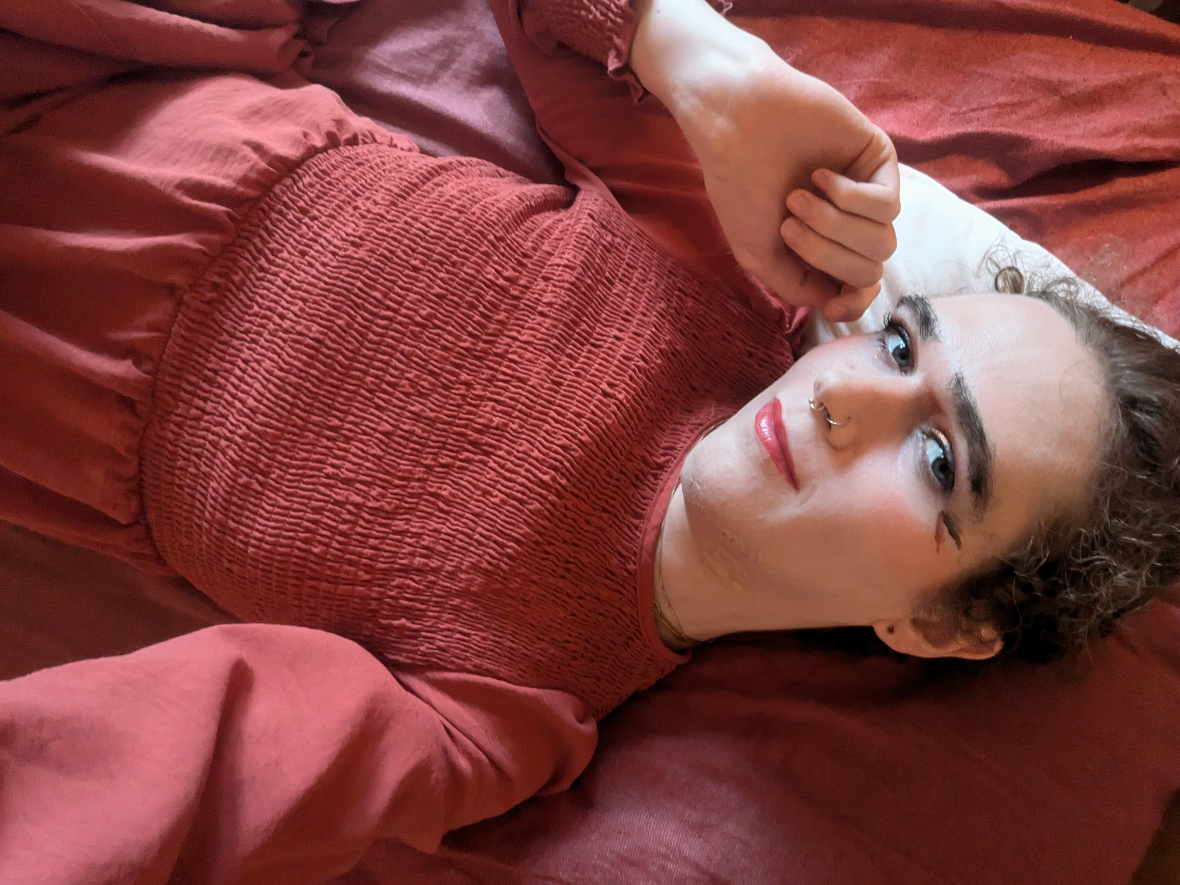 The photo shows a woman lying down on a bed with red sheets and... - by Daisy