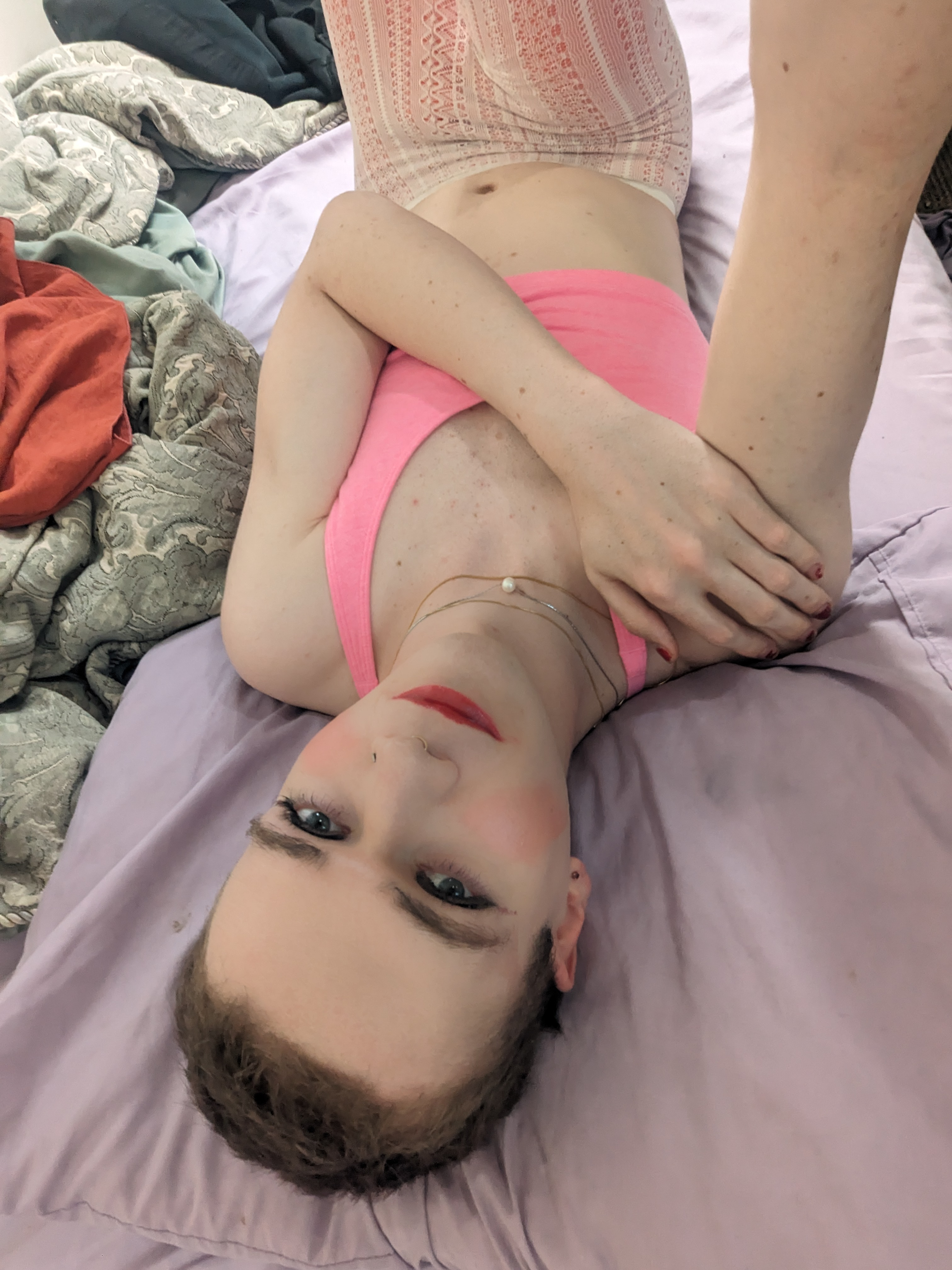 The photo shows a woman lying on a bed with light purple sheets.... - by Daisy