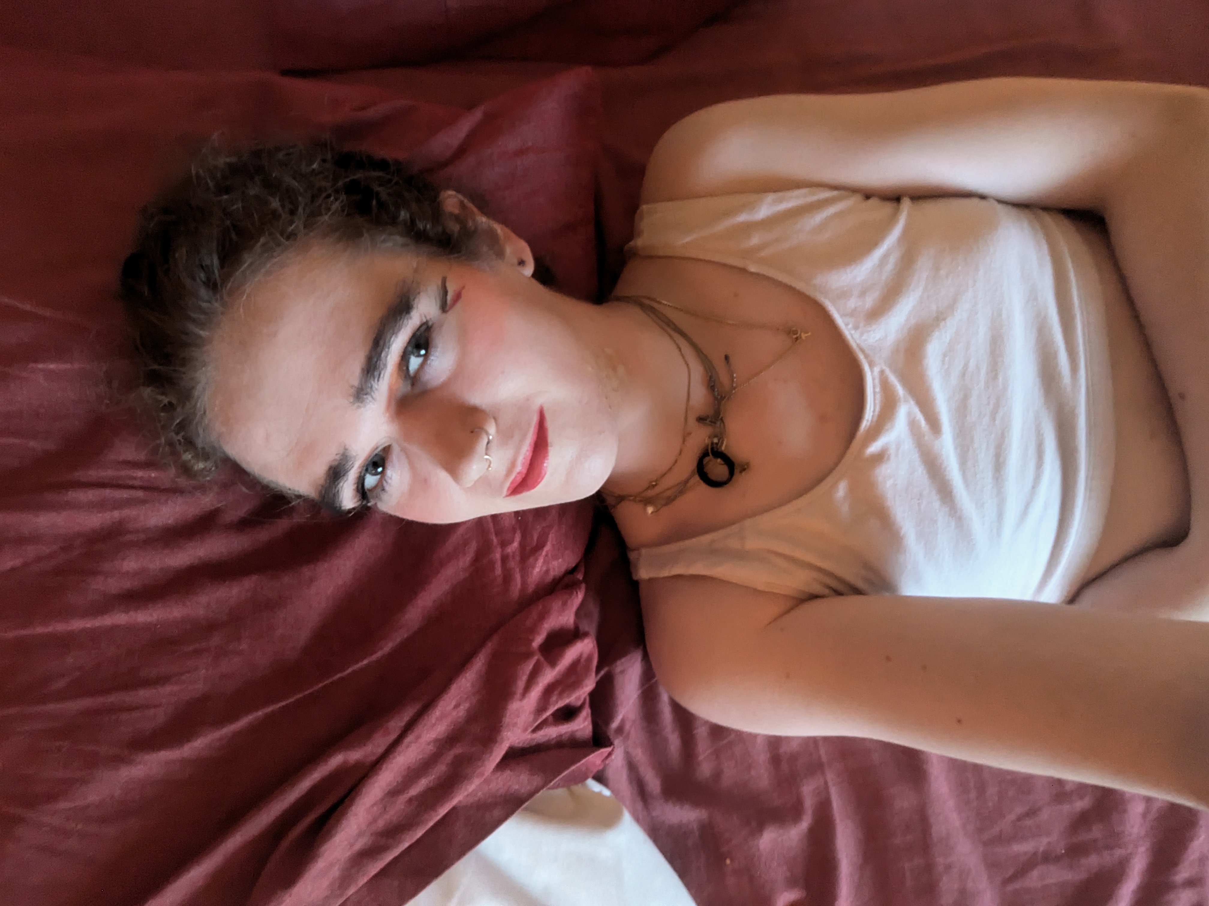 This photo shows a woman lying down on a bed with a maroon sheet.... - by Daisy