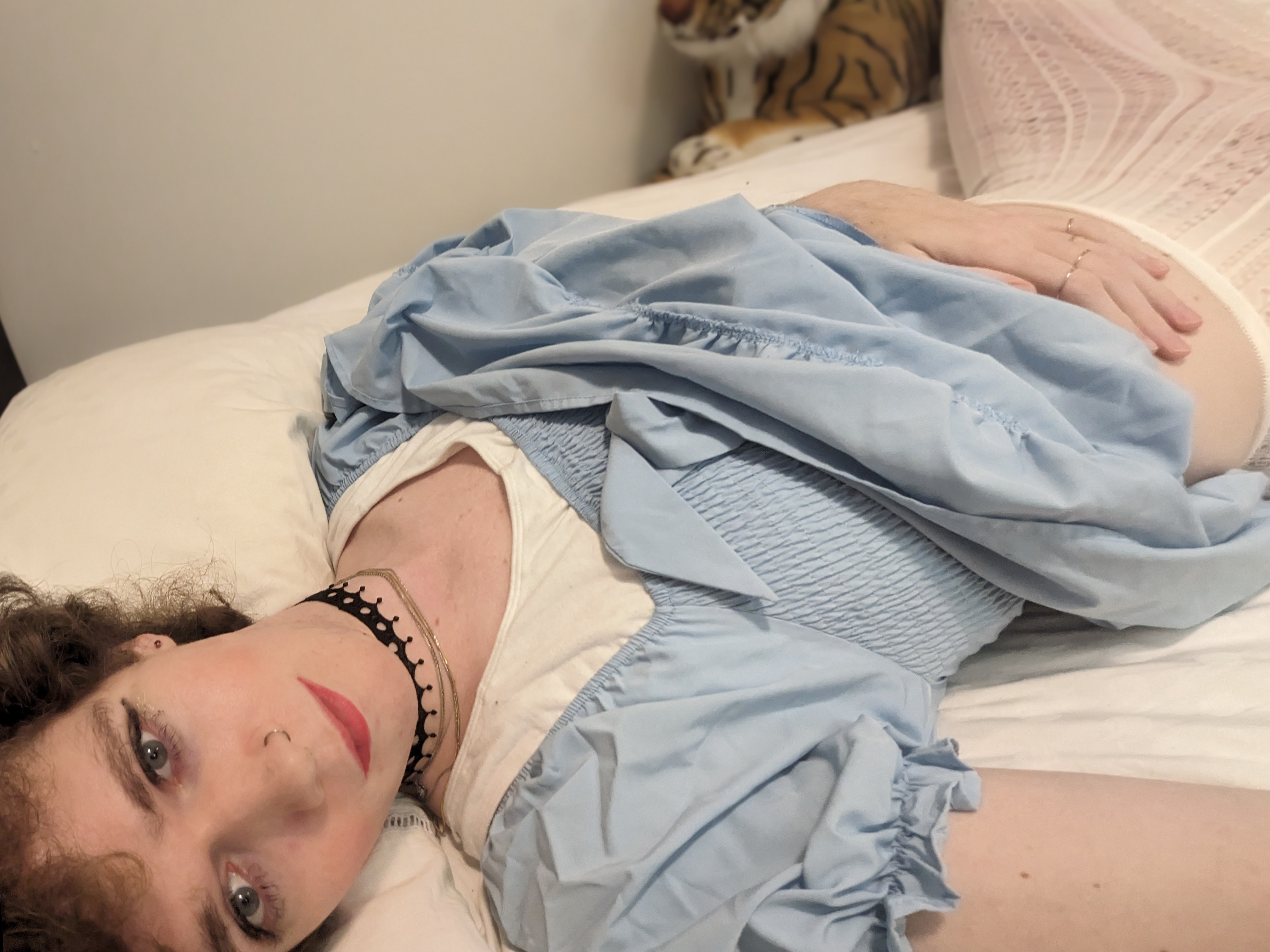 The photo shows a woman lying on a bed. She has curly hair and is... - by Daisy