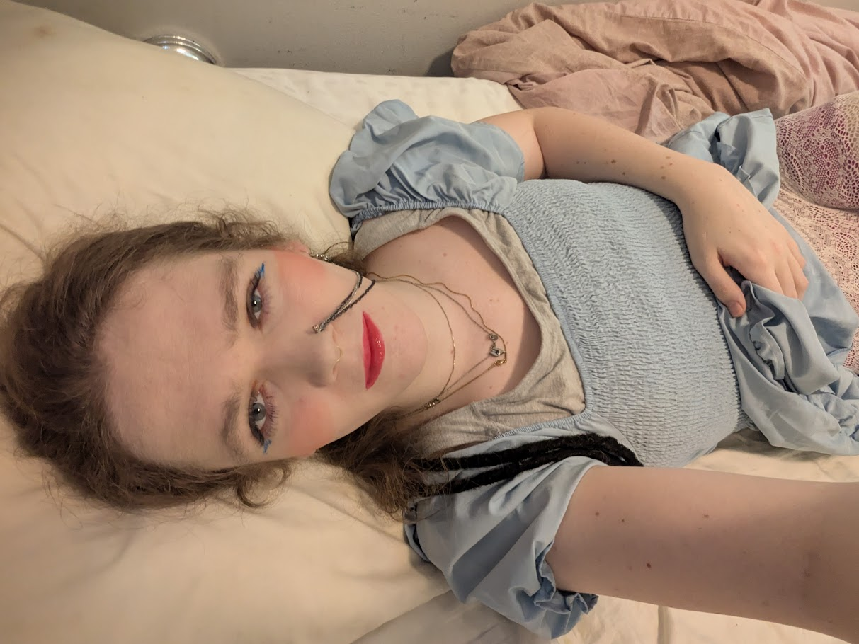 The photo shows a woman lying on a bed, looking up at the camera....